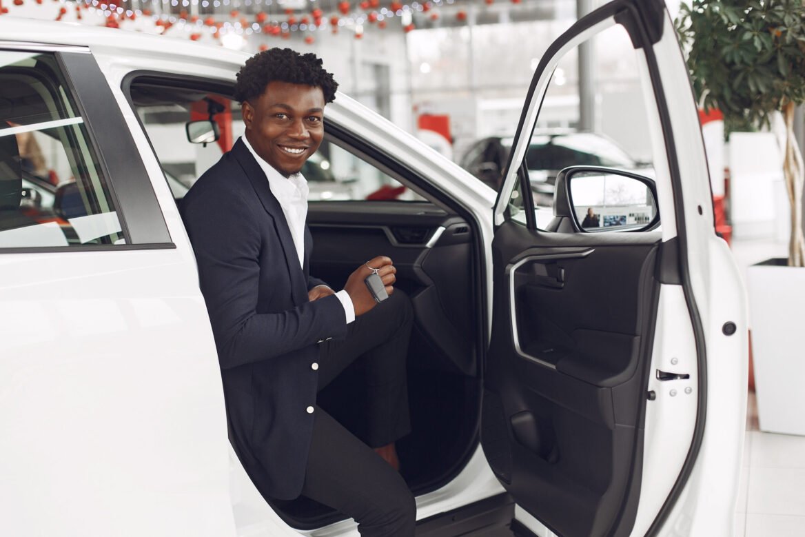 Man buying the car. Businessman in a car salon. Black male in a suit.